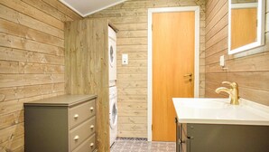 Ein kleines Badezimmer mit Holzwänden, einem weißen Waschbecken und einer integrierten Waschmaschine.