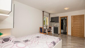 Een slaapkamer met een bed, een eettafel en een kitchenette op de achtergrond.