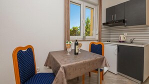 Een kleine kitchenette met een raam, een tafel met tafelkleed, twee stoelen en een fles wijn op de tafel.
