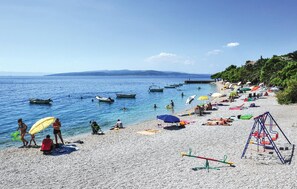 Una spiaggia con acque cristalline, barche, ombrelloni e persone.
