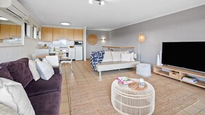 Een moderne woonkamer met een bank, een ronde salontafel, een televisie en een keuken op de achtergrond.