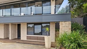 Een modern huis met twee verdiepingen, een balkon, grote ramen en een gevel van natuursteen.