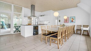 Eine moderne Küche mit weißen Schränken, einer Edelstahl-Dunstabzugshaube und einem Essbereich mit Holzkohle-Stühlen und einem Glastisch.