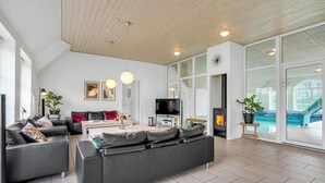Ein geräumiges Wohnzimmer mit einer großen Couch, einem Fernseher und einem Kamin. Eine Glastür führt zu einem Poolbereich.