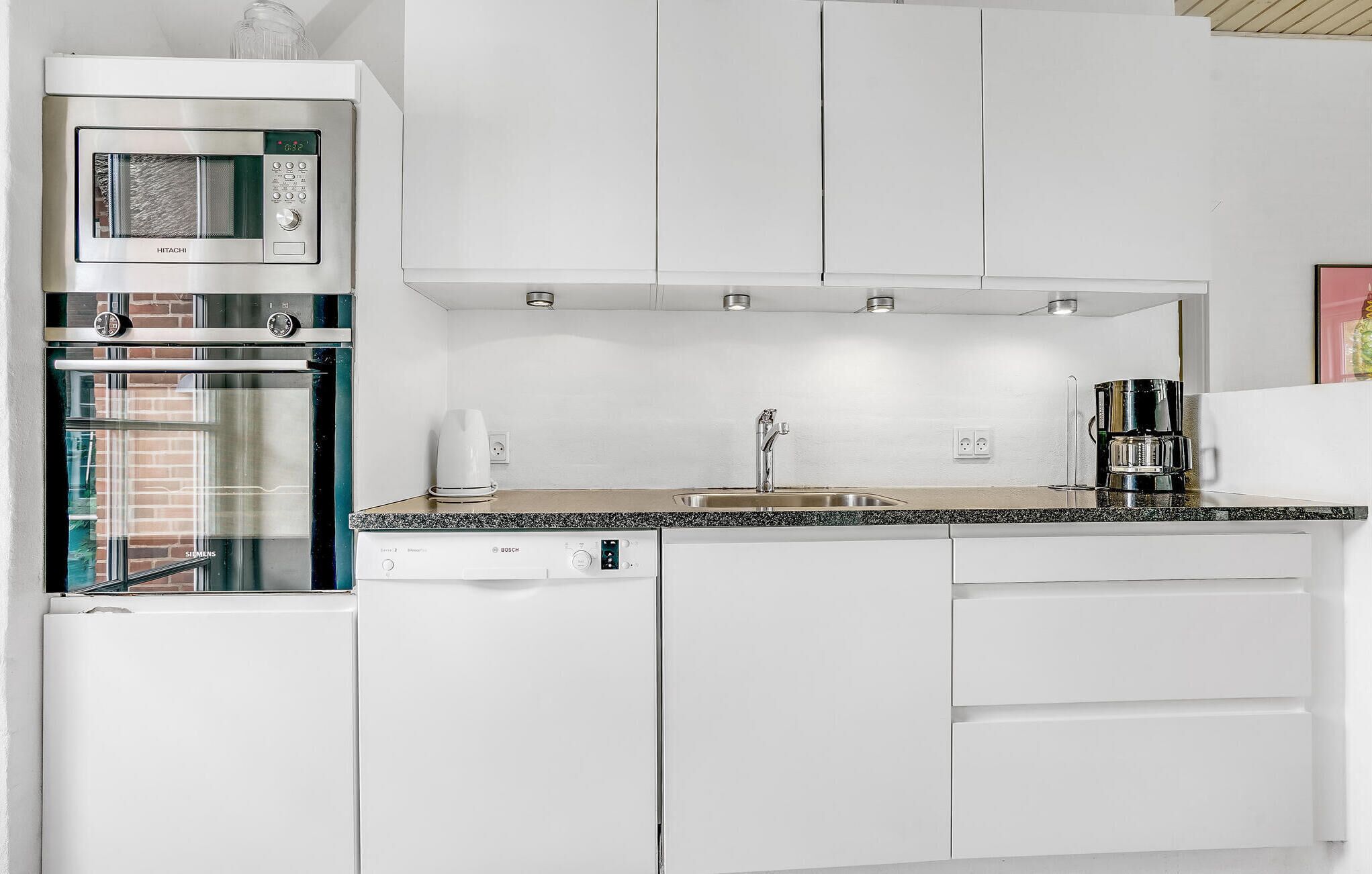 A modern kitchen with white cabinets, a built-in microwave, a Bosch dishwasher, and a coffee maker.
