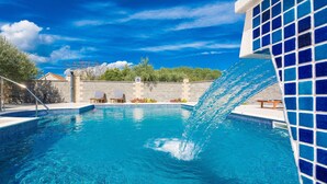 A swimming pool with a clear blue water feature, two lounge chairs, and a stone wall in the background. - Awesome apartment in Biograd na moru (Biograd na moru)