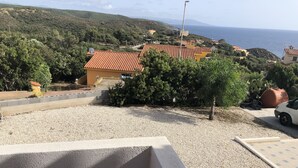 Ett bostadsområde med ett hus som har ett rött tegeltak, omgivet av grönska och med utsikt över havet.