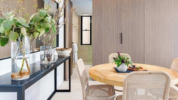 A modern dining area with a round wooden table, wicker chairs, and potted plants.