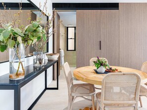A modern dining area with a round wooden table, wicker chairs, and potted plants.