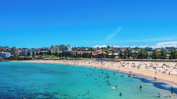 A beach with clear turquoise water, a sandy shore, and buildings in the background.