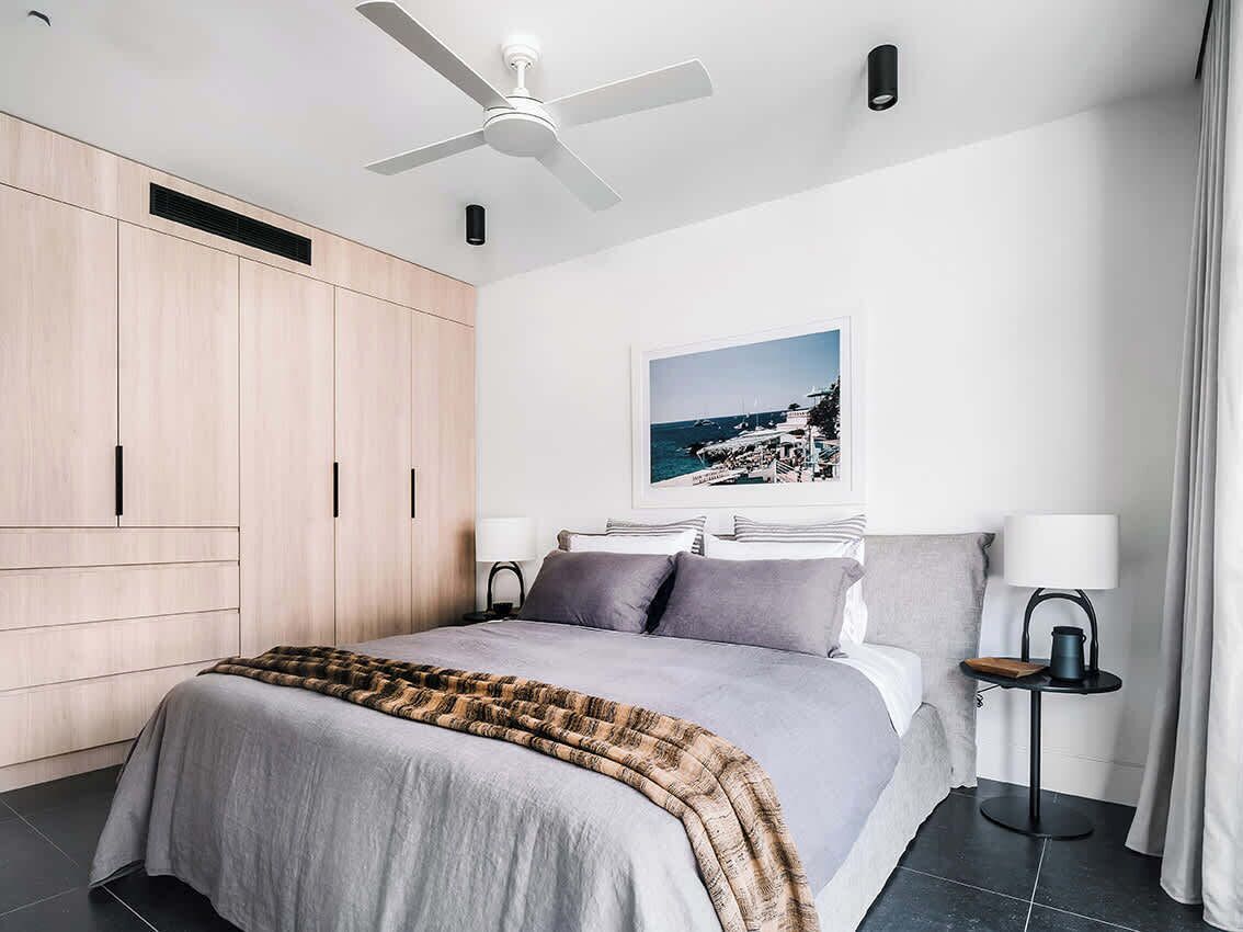 A modern bedroom with a bed, a ceiling fan, a nightstand, a lamp, and a framed picture on the wall.