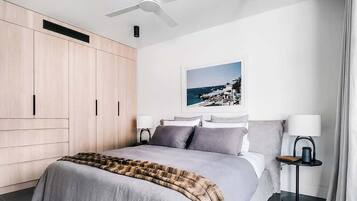 A modern bedroom with a bed, a ceiling fan, a nightstand, a lamp, and a framed picture on the wall.