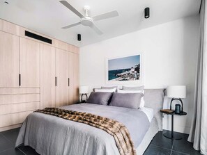 A modern bedroom with a bed, a ceiling fan, a nightstand, a lamp, and a framed picture on the wall.