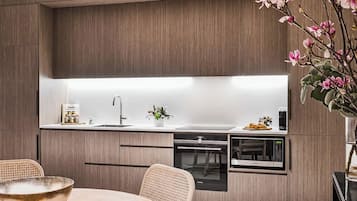 A modern kitchen with wood paneling, a built-in oven, microwave, and a dining area with a table and chairs.