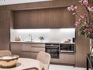 A modern kitchen with wood paneling, a built-in oven, microwave, and a dining area with a table and chairs.