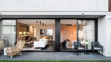 Une maison moderne dotée d’un balcon, d’un salon avec un canapé et des fauteuils, d’un coin repas avec une table et des chaises, et d’une cuisine visible à travers des portes vitrées.