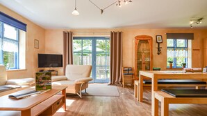 A spacious living room with a sofa, a coffee table, a TV, and a dining area with a wooden table and chairs.