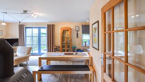 A modern living room with a sofa, a dining table with a bench, a TV, and a large window with curtains.