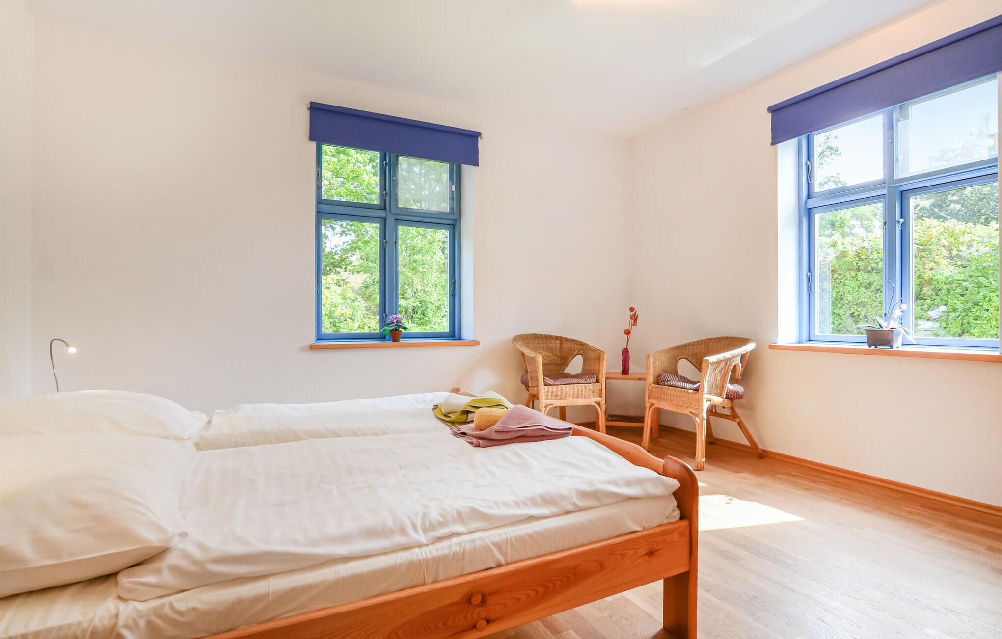 A bedroom with two beds, a chair, and two windows with blue shutters.