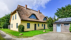 A two-story house with a thatched roof, a small attached wooden structure, and a well-maintained lawn.