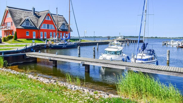 A marina with boats docked, a wooden pier, and a red house with a thatched roof.