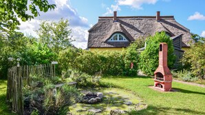 A traditional house with a thatched roof, a garden with a pond, and a red oven.