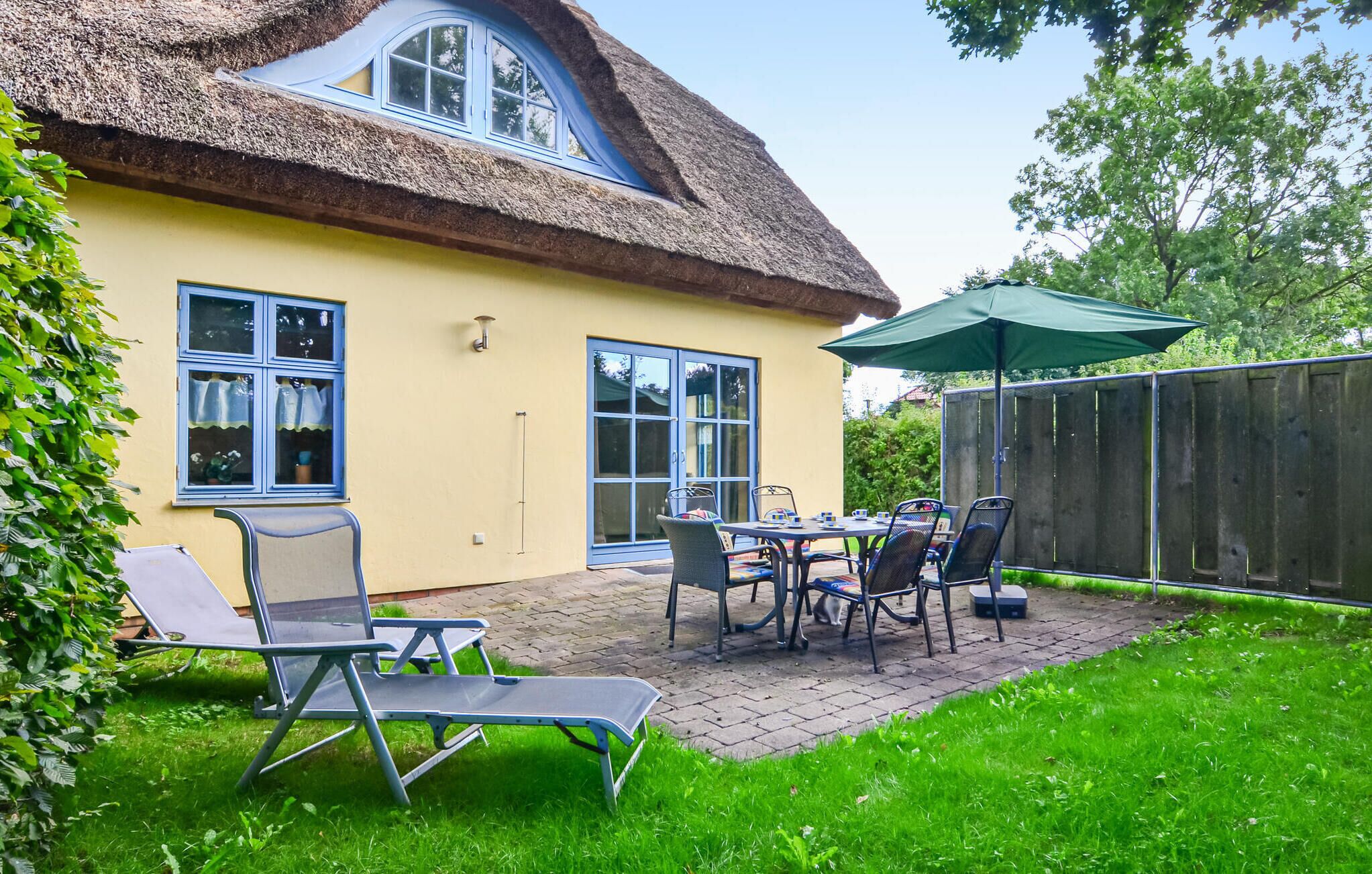 A house with a thatched roof, a patio with a table and chairs, and a fenced yard.