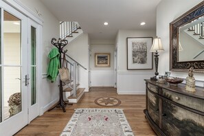 A hallway with a staircase, a patterned rug, a cabinet with decorative items, and a framed picture on the wall.