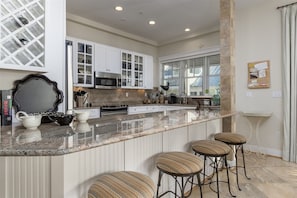 A kitchen with white cabinets, a granite countertop, and a bar area with stools. - Sunset Island 8 Beach Side Mews (Ocean City)