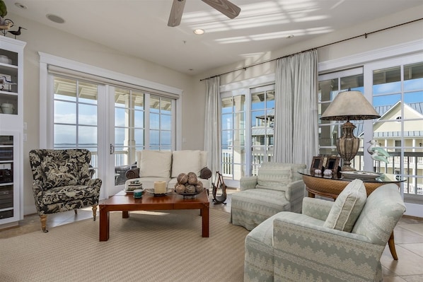A spacious living room with a large window, a ceiling fan, and a coffee table with decorative items. - Sunset Island 8 Beach Side Mews (Ocean City)