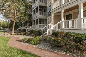 A multi-story building with a brick pathway leading to a white porch with railings.