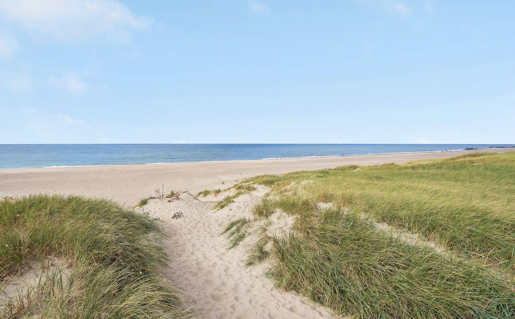 Une plage de sable avec des dunes herbeuses qui s’étendent jusqu’à l’océan.