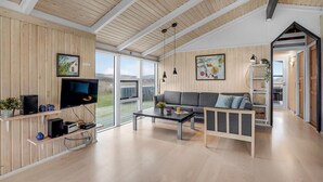A modern living room with a wooden ceiling, a grey sofa, a coffee table, and a TV on a wooden shelf. - Cozy home in Harboøre with sauna (Harboøre)