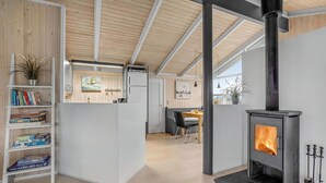 A modern interior with a wooden ceiling, a fireplace, a dining area, and a bookshelf. - Cozy home in Harboøre with sauna (Harboøre)