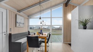 A modern dining area with a wooden table, black chairs, and a bench. Large windows offer a view of the outdoors. - Cozy home in Harboøre with sauna (Harboøre)