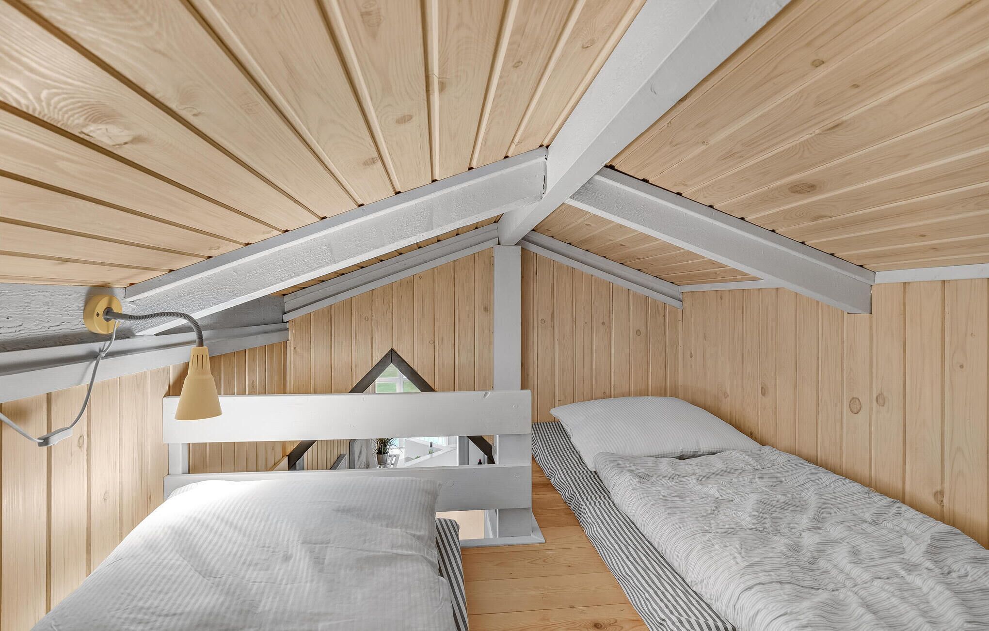 Una habitación compacta de estilo cabaña, con dos camas, techo inclinado y un ventanal pequeño.