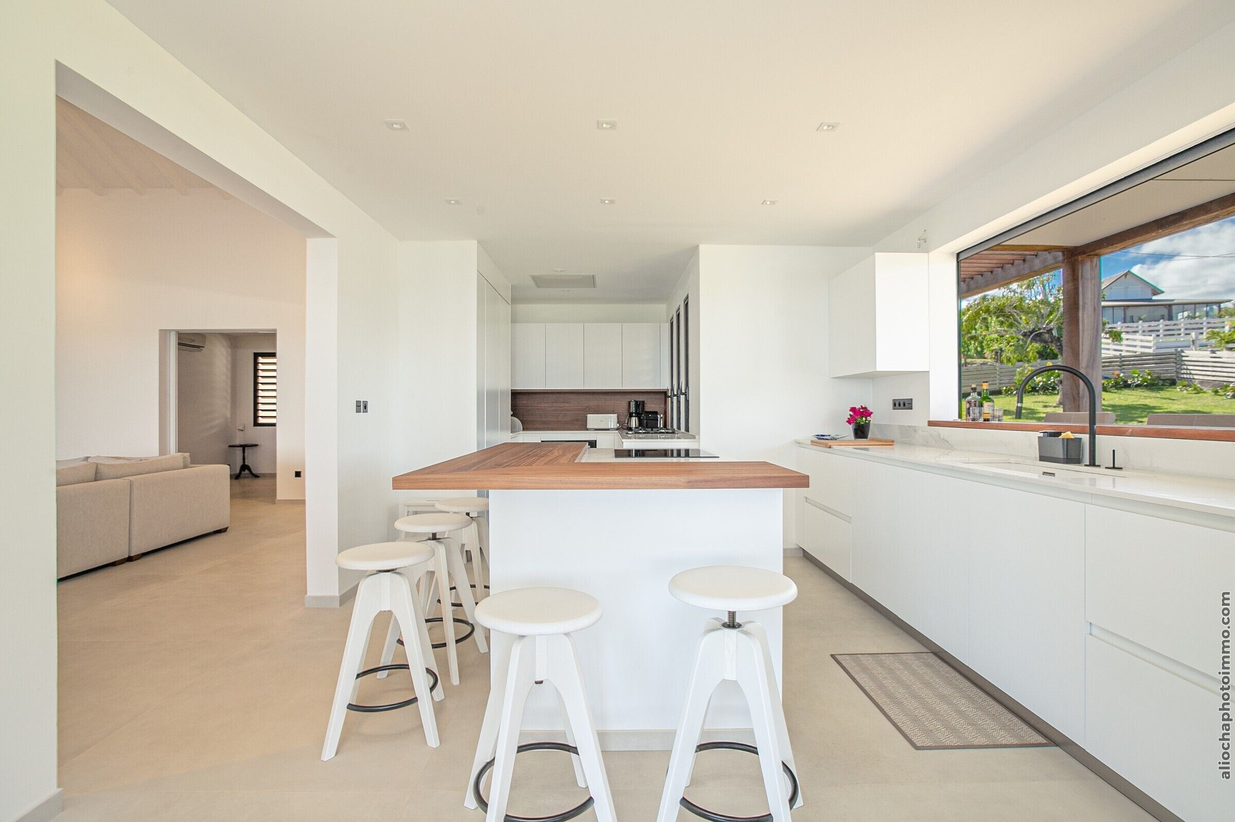 A modern kitchen with white cabinetry, a wooden countertop, and three white stools.