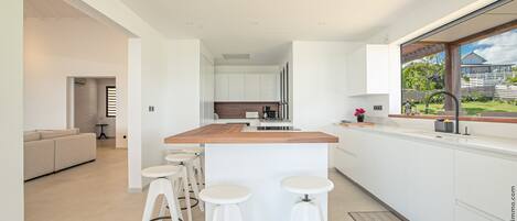 A modern kitchen with white cabinetry, a wooden countertop, and three white stools.