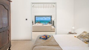 A bedroom with a bed, a bedside table, a nightstand, a wooden wardrobe, and a view of the sea through a glass door.