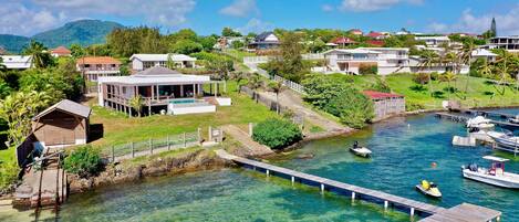 A coastal residential area with clear waters, a dock, and houses with large windows overlooking the water.