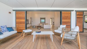 A spacious living area with a wooden floor, white furniture, and a view into the adjacent room.