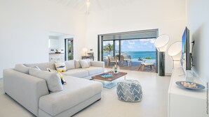A modern living room with a large sectional sofa, a coffee table, and a view of the ocean through large windows.