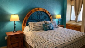 Ein Schlafzimmer mit einem großen Bett, zwei Nachttischen mit Lampen, einem Holzkopfstück und einem Fenster mit Vorhängen.