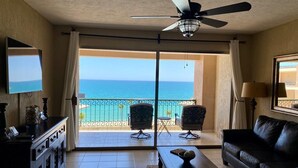 Ein Zimmer mit Deckenventilator, Fernseher, Sofa, Couchtisch und Meerblick durch eine Schiebetür.