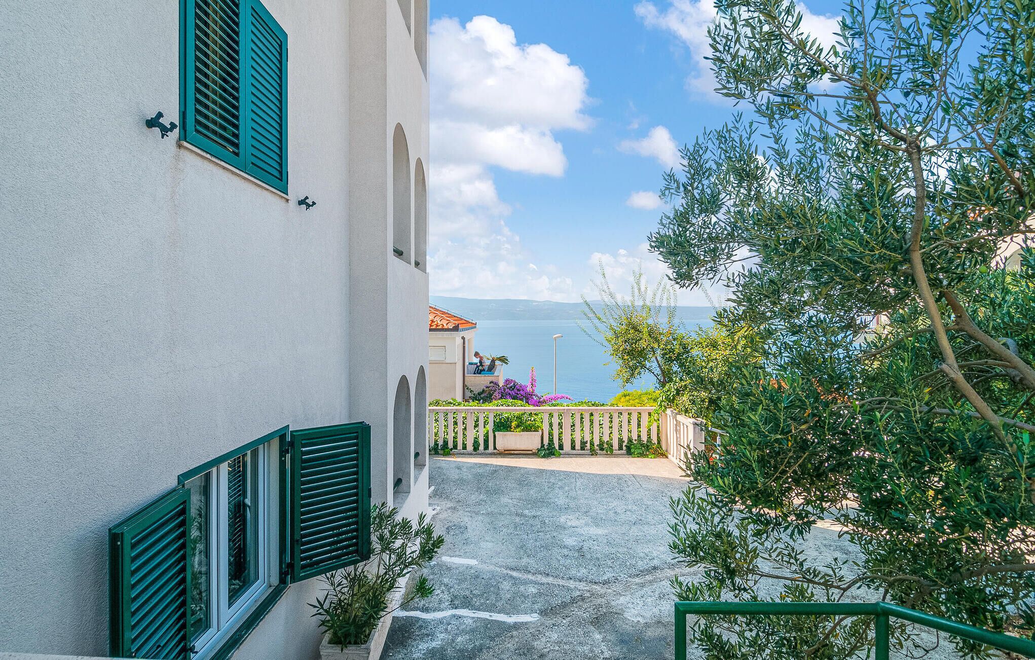 A narrow pathway leading to a building with green shutters and a view of the sea.