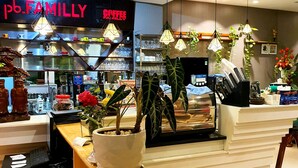 A coffee shop interior with a reception desk, potted plants, hanging lights, and a visible menu board.