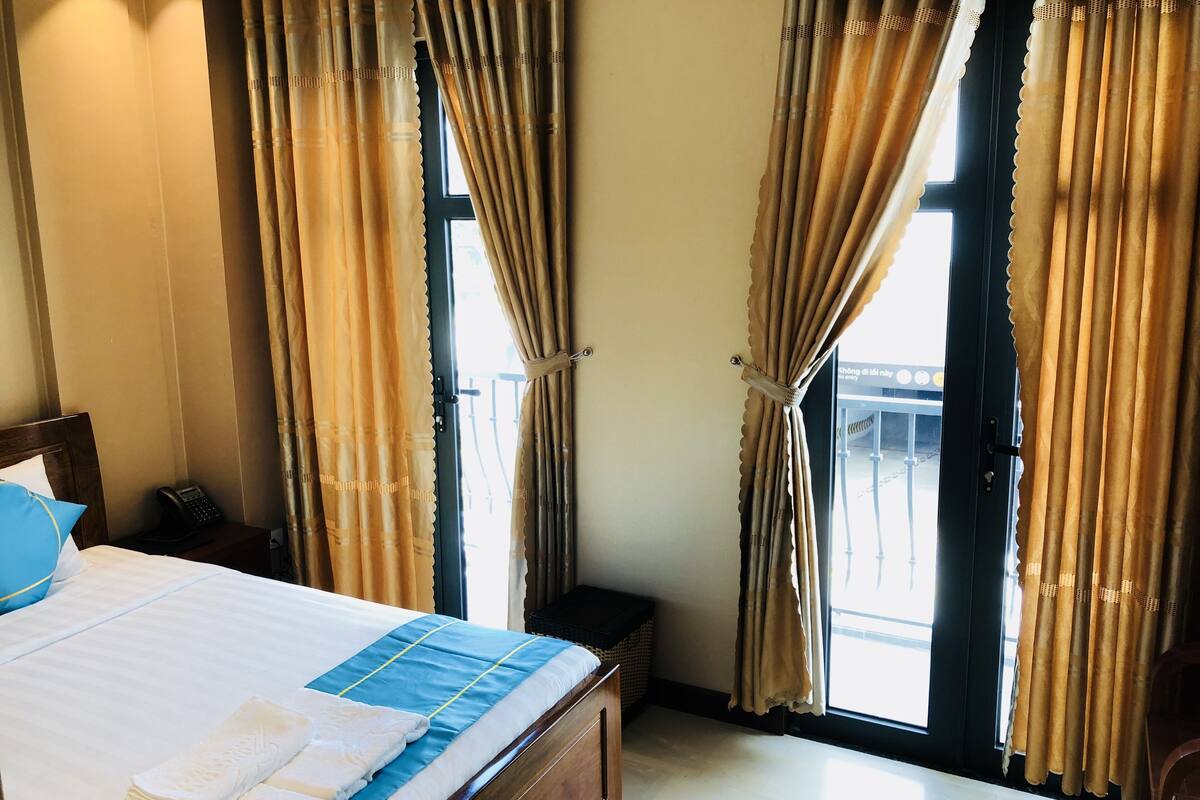 A hotel room with a bed, a bedside telephone, and a window with curtains.