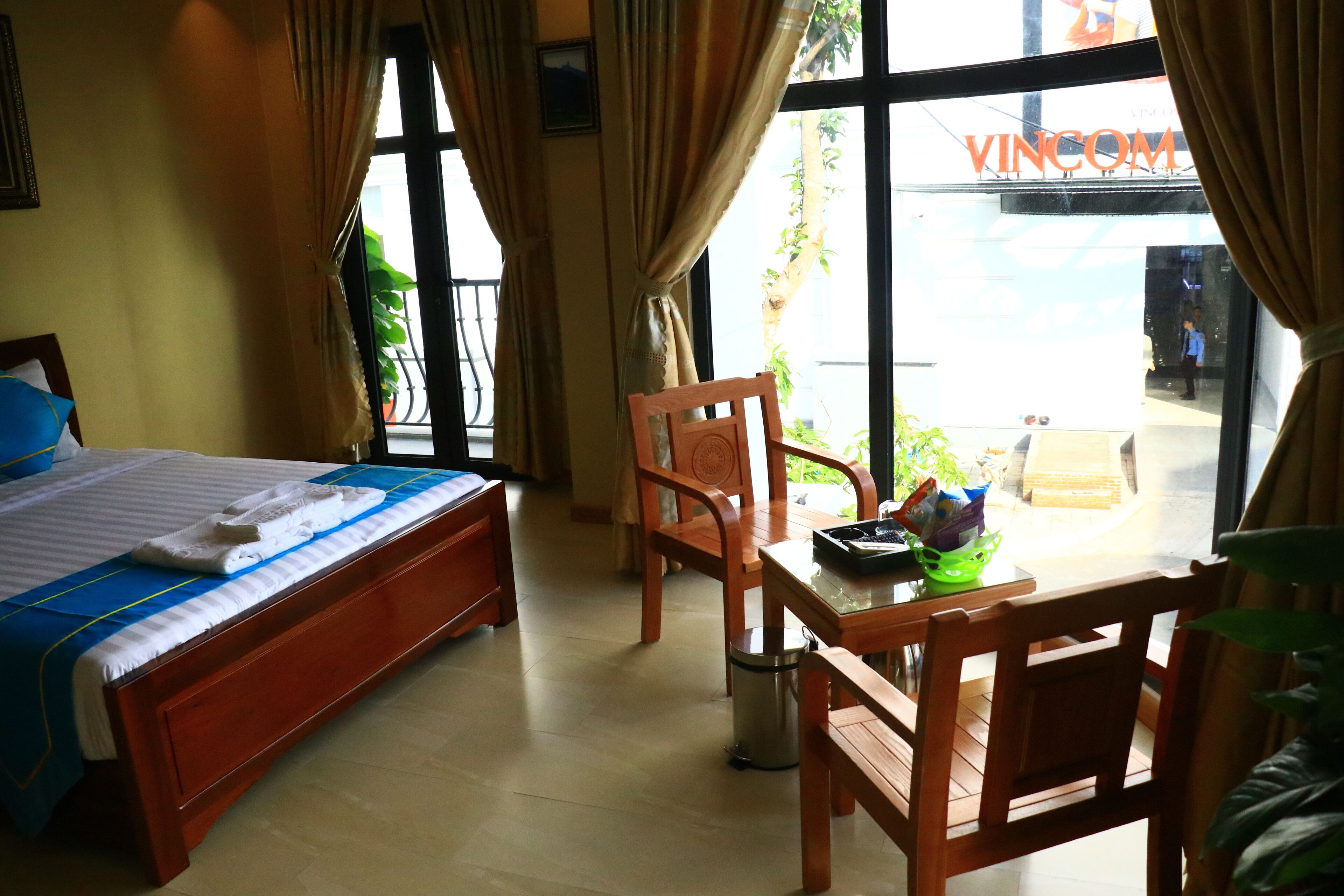 A hotel room with a bed, a wooden table with chairs, a window with curtains, and a view of the outside.