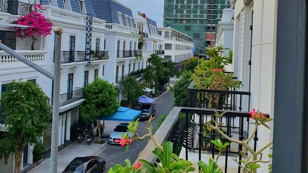 A street view with a hotel named "ELITE HOME HOTEL" on the left, a modern building under construction in the background, and a balcony with potted plants.