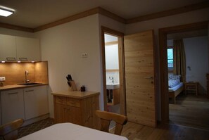Een kamer met een bed, een houten deur, een kleine tafel en een kitchenette.